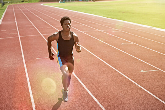 Fitness, man and college student running on track with speed exercise, cardio training and practice. Bokeh, black person or athlete outdoor at university with sports scholarship, workout or wellness.