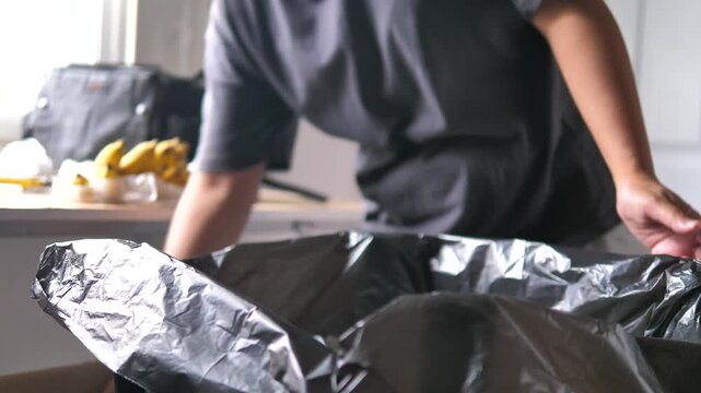 Close-up view of a person placing a plastic bottle into a waste collection bag, Household waste sorting and responsible disposal practices