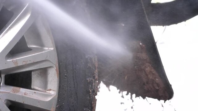 Close-up view of a car tire and alloy wheel with visible dirt, mud, and water spray, highlighting vehicle maintenance