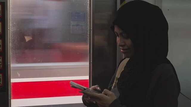 Muslim woman in hijab using smartphone on a moving train