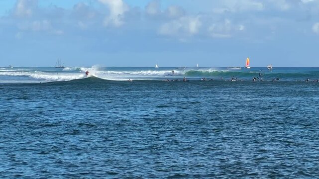 Ala Moana Bowls surfing in Waikiki Honolulu Hawaii, crowded ocean lineup with surfers riding waves and background sailboats, real-time.