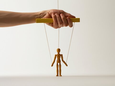 Human hand manipulating wooden marionette puppet strings against