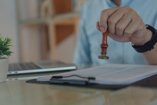 Hand holding document stamp above paperwork beside laptop for business approval authorization compliance and administrative verification process
