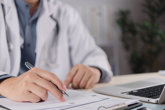 Healthcare professional reviewing medical paperwork with pen beside laptop and stethoscope for clinical administration documentation workflow