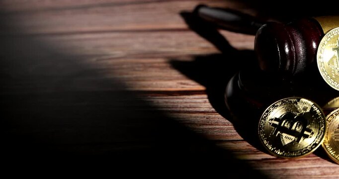 Tracking horizontal movement showcasing a wooden gavel of authority positioned beside physical golden bitcoin coins on dark background during legal trial.