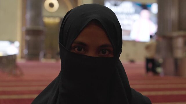 Muslim woman wearing niqab looking at camera in mosque