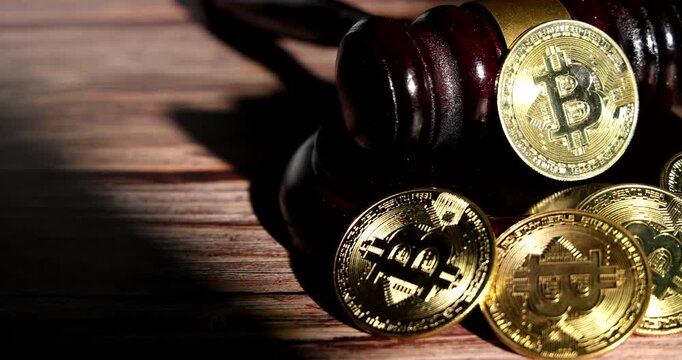Slow tracking movement over a wooden gavel and shiny gold bitcoin coins placed together on desk, representing cryptocurrency legislation and regulation.