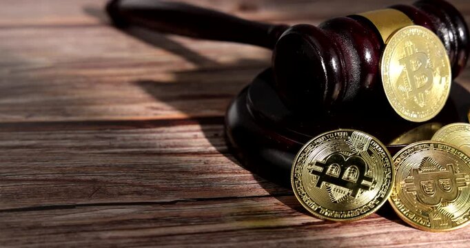 Horizontal tracking camera movement across a wooden judge gavel standing next to a pile of golden bitcoin physical coins on a dark wooden surface in court.
