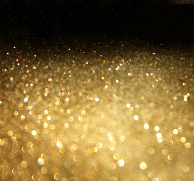 Close up view of golden glitter texture with soft focus and deep bokeh light spheres on dark background