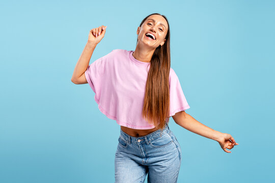 Happy young woman dancing, laughing on blue background