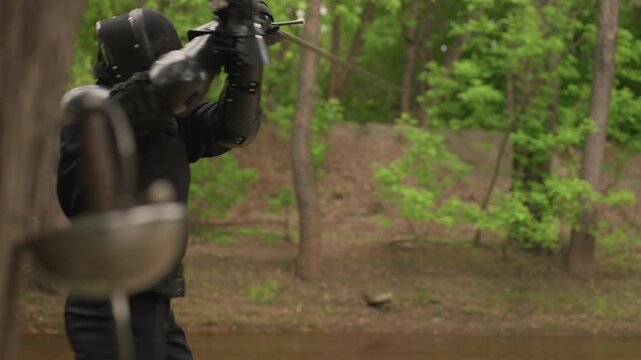 Close up of person in black fencing gear actively engaging with another fencer demonstrating sword techniques and movements. scene features interaction between two people using swords