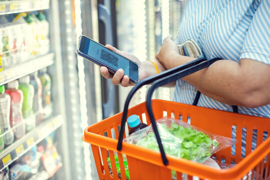 Selective focus to Woman scanning QR code with smartphone while holding shopping basket in supermarket