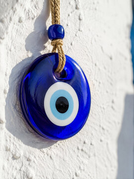 Traditional blue evil eye (Nazar) glass amulet hanging on a textured white Mediterranean wall
