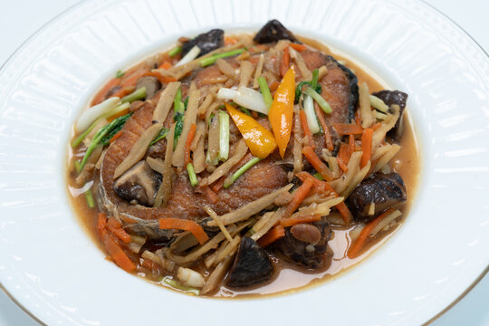 Close-up, Fried mackerel topped with stir-fried chili and ginger sauce (ginger, shiitake mushrooms, carrots, scallions) in a white dish.