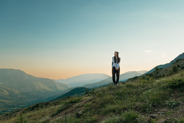 Obraz premium Young female hiker standing on a grassy mountain ridge enjoying the scenic valley view at sunset in Verri, Albania