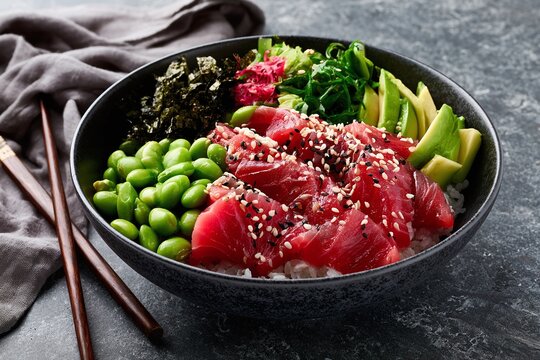 Colorful Hawaiian poke bowl with raw tuna avocado edamame and seaweed on dark slate surface