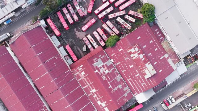 Aerial drone view of a dense industrial area featuring large warehouse buildings, factory rooftops, surrounding roads, vehicles, trees, and urban infrastructure. The composition highlights the contras