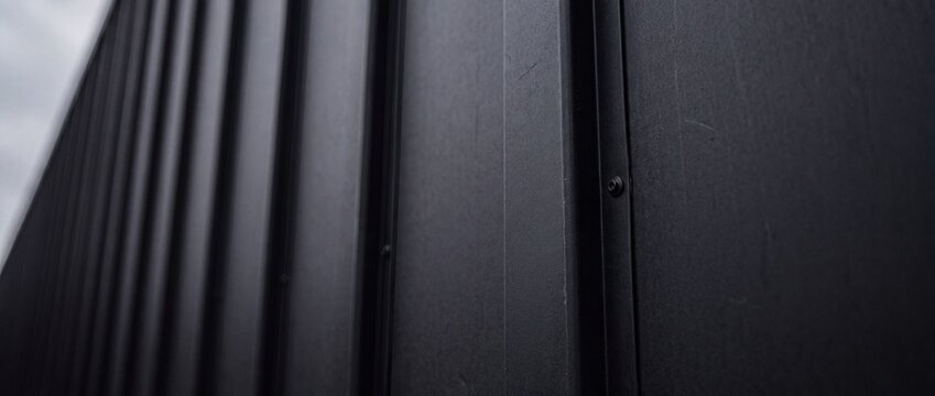 Black corrugated metal siding panel detail with vertical lines and industrial fastening bolts for modern exterior cladding architecture