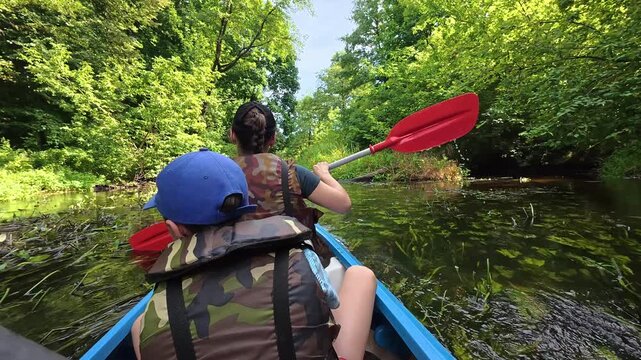 People paddling in a kayak on a narrow river through a lush green forest. Summer adventure family Kayak trip. Active lifestyle, weekend pastime. Outdoor recreation. High quality 4k footage.