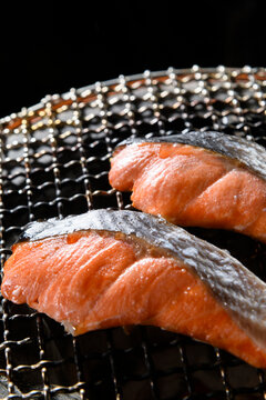 Grilled salmon fillets cooking on a traditional shichirin charcoal grill, sprinkled with sea salt, showing beautiful char marks and moisture from the Japanese BBQ cooking process