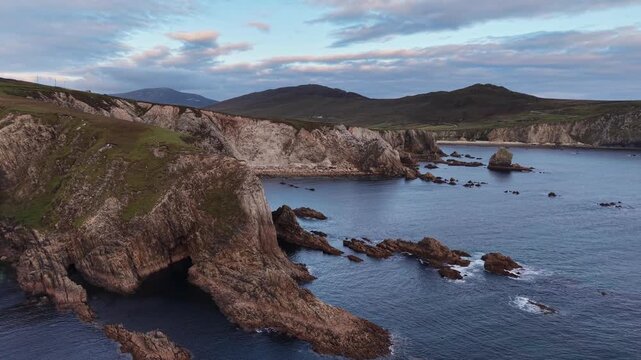 Coastline with rocky formations no visible action static scene, in seaside landscape at dusk or early evening, with rocky cliffs, ocean water, sky with clouds, with blue, gray accents.