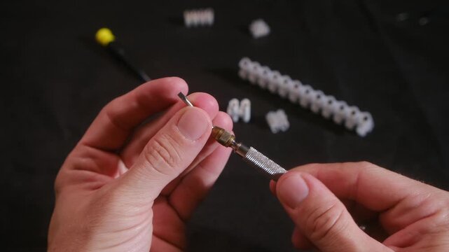 Close up hands changing bit on universal metal screwdriver, switching cross to flat. Terminal strip and electrical components on dark table. Hands changing bit on universal metal screwdriver close up 