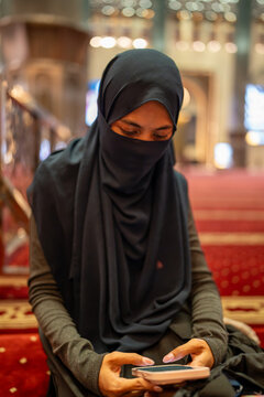 Muslim woman wearing a niqab using a smartphone inside a mosque