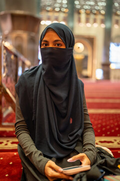 Muslim woman wearing niqab and hijab using phone in mosque