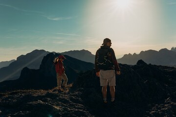 Man and child stand on a ridge watching sunrise over the Dolomite peaks. Family hiking and shared sunrise for travel, parenting and outdoor lifestyle themes © Екатерина Лукашина