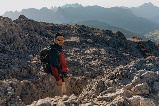 Man with a backpack looks back over his shoulder on a sunlit rocky mountain ridge. Adventure spirit and discovery on the trail for travel, backpack gear and outdoor marketing