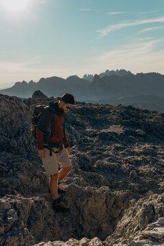 Man with a backpack hikes down a rocky mountain ridge under a bright hazy sky. Mountain trekking and endurance for adventure travel, fitness and outdoor gear marketing