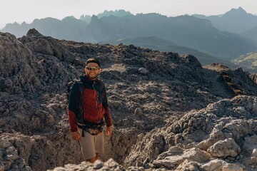 Man with a backpack stands on a rocky ridge before hazy layered Dolomite mountains. Solo trekking and wanderlust in the mountains for travel, gear and outdoor lifestyle marketing © Екатерина Лукашина