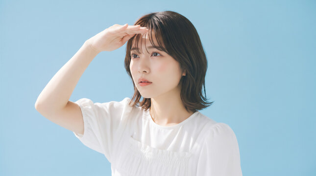 Young Japanese woman looking into the distance with hand shading eyes against blue background