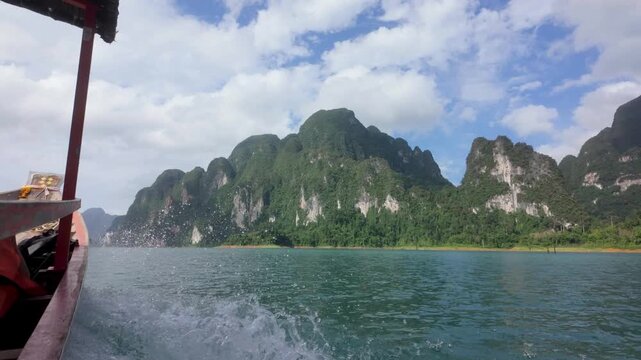 Boat on Cheow lan lake in Khao Sok National Park, Slow motion shot from the boat showing the spray and wake of the water with jungle and dramatic limestone cliffs as the backdrop. 