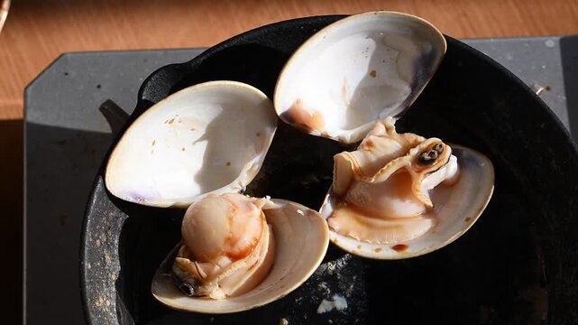 網焼きでぐつぐつと沸騰する醤油と湯気が立つ大粒のハマグリ