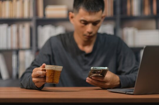 Man reading smartphone and drinking coffee in a library with bookshelf background