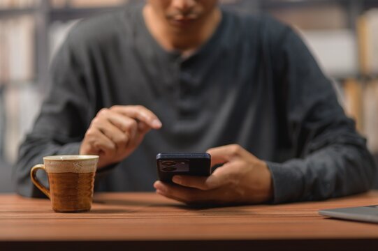 Person Using Smartphone with Coffee Mug on Wooden Table in Cafe Setting