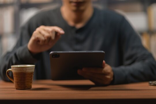 Person Using Digital Tablet at Wooden Table with Coffee Mug in Indoor Setting