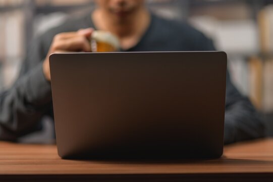 Person Using Laptop Computer and Drinking Coffee in a Cozy Workspace