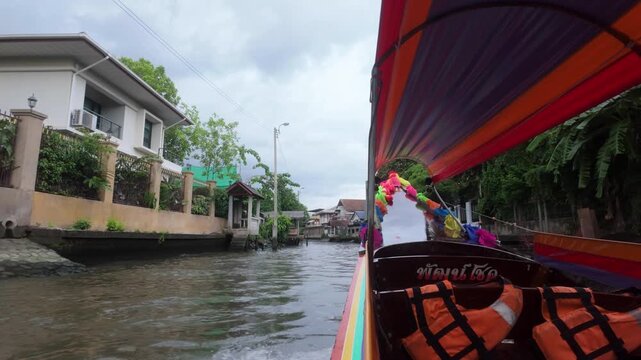 Long-tail boat travelling through a narrow canal in Thailand. POV shot from passenger. Waterway, houses on stilts. Location: Thonburi, Bangkok &mdash; canal near Wat Paknam Phasi Charoen and Golden Buddha.