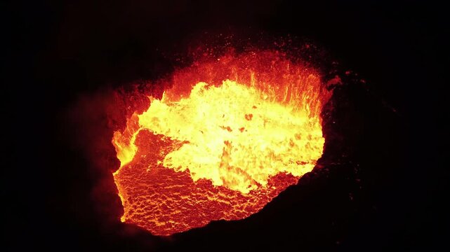 Close-up of the crater of an erupting volcano spewing lava at night.
