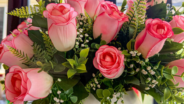 Close-up of decorative artificial pink rose bouquet with green foliage and small white flowers, floral arrangement for interior decor.