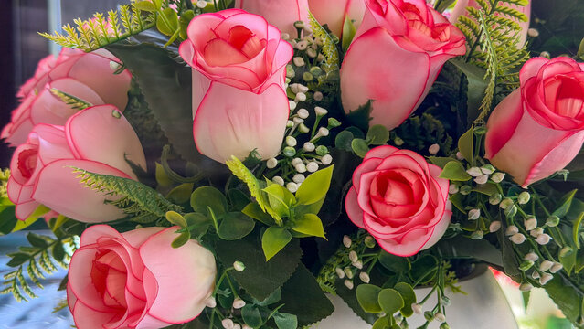 Close-up of decorative artificial pink rose bouquet with green foliage and small white flowers, floral arrangement for interior decor.