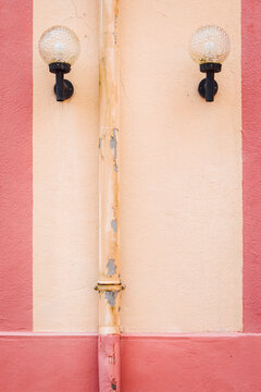 Luminaires sur un mur rose et cr&egrave;me avec un ch&eacute;neau descendant. Mur graphique. Lampes ext&eacute;rieures sur une fa&ccedil;ade. Appliques vintage
