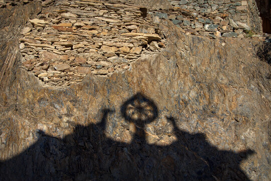 Shadow of Buddhist temple roof with Dharmachakra symbol on stone wall in Ladakh