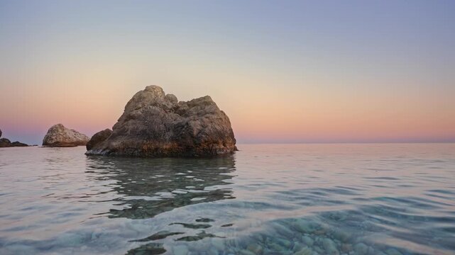 Calm sea waves ripple near majestic coastal rock formations during a warm pastel sunset. Real time meditative water footage benefits hotel website headers or travel vlogs as a design element.