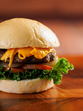 Delicious cheeseburger layer with golden bun juicy meat beef or pork patty melted cheddar cheese on wooden table background fresh ingredients green lettuce tomatoes tasty classic burger junk fast food