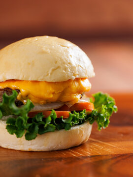 Delicious cheeseburger layer with golden bun juicy meat beef or pork patty melted cheddar cheese on wooden table background fresh ingredients green lettuce tomatoes tasty classic burger junk fast food