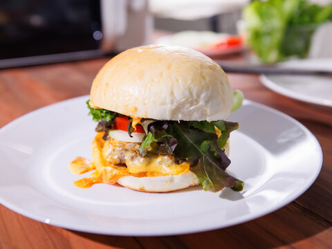 Delicious cheeseburger on plate layer with golden bun juicy meat beef or pork patty melted cheddar cheese on wooden table background fresh ingredients lettuce tomatoes tasty classic burger junk food
