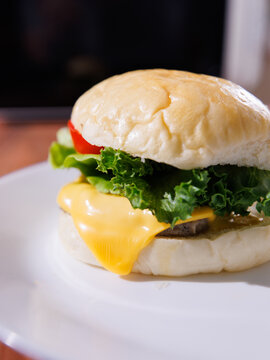 Delicious cheeseburger on plate layer with golden bun juicy meat beef or pork patty melted cheddar cheese on wooden table background fresh ingredients lettuce tomatoes tasty classic burger junk food
